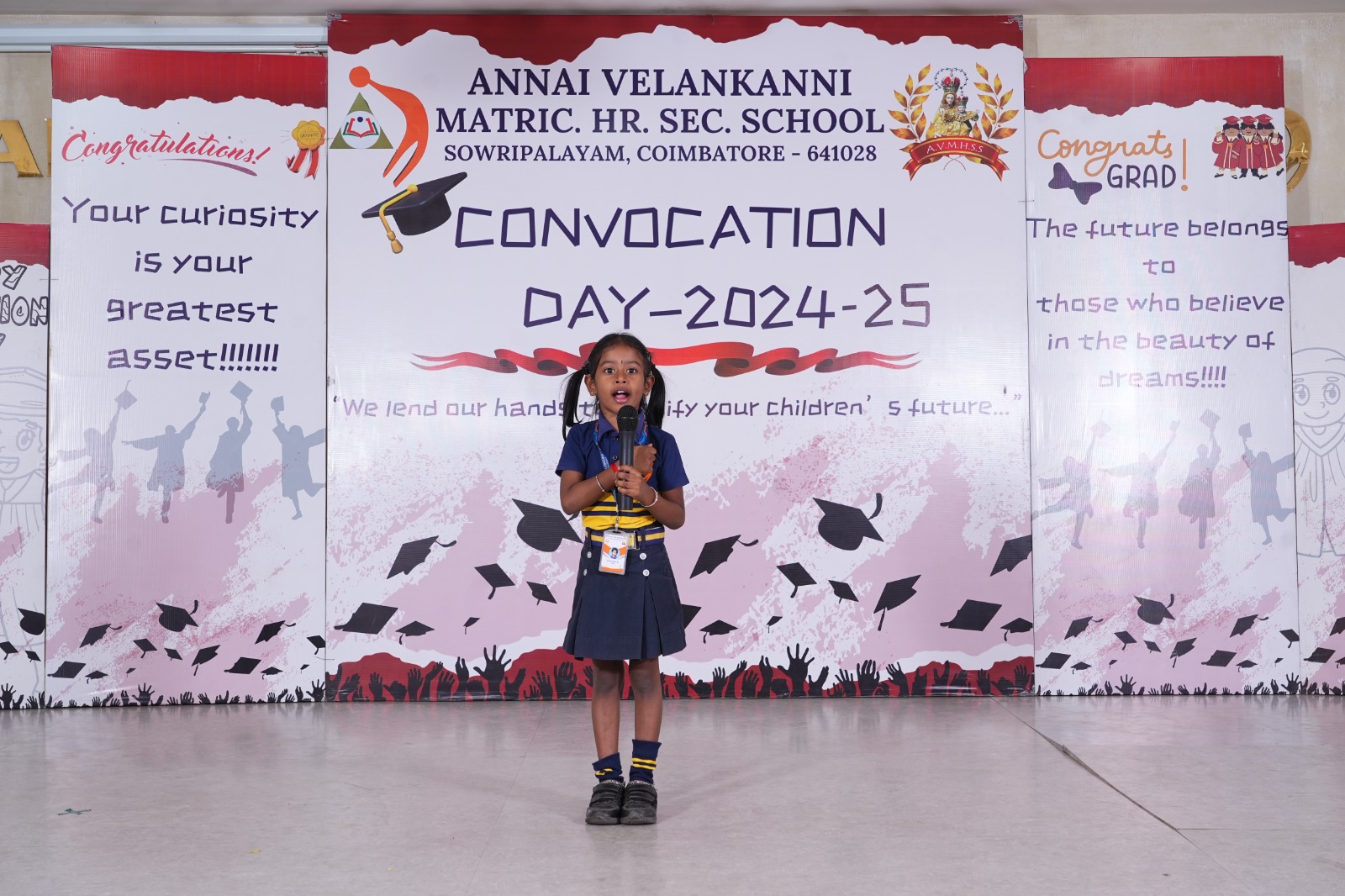 A student speaking confidently at the microphone during a school event at Annai Velankanni, Sowripalayam, Coimbatore